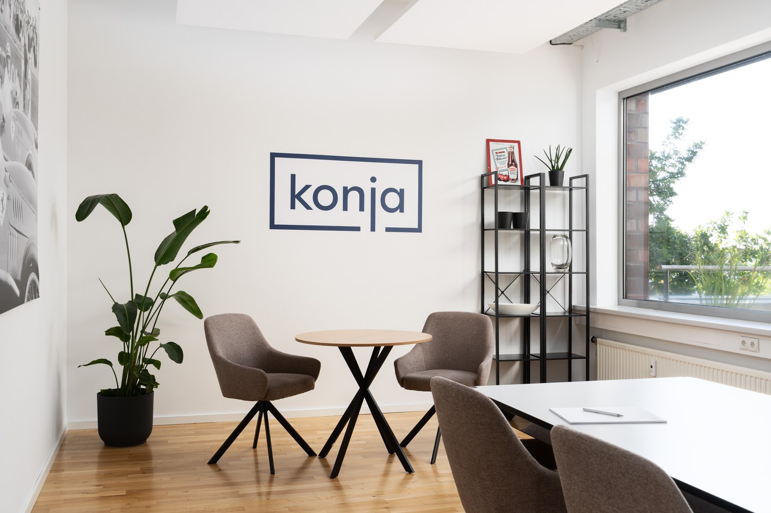 Gesprächsbereich mit Sesseln, Holztisch und konja-Logo an der Wand.